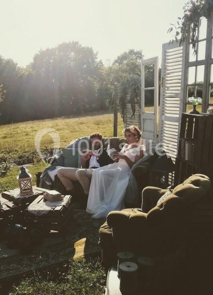 Un couple assis sur un canapé en extérieur, entouré de décorations rustiques, lisant sous une lumière douce.
