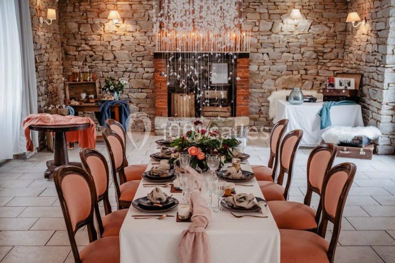 Salle décorée avec une table élégante pour un repas, entourée de chaises, avec un mur en pierre et des lumières tamisées.