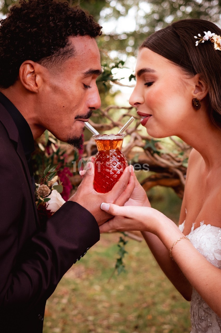 Un couple partage une boisson dans un verre en forme d'ananas lors d'une célébration en plein air.