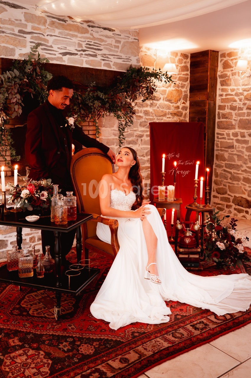 Un couple en tenue de mariage dans un décor chaleureux avec bougies, tapis et mur en pierre.