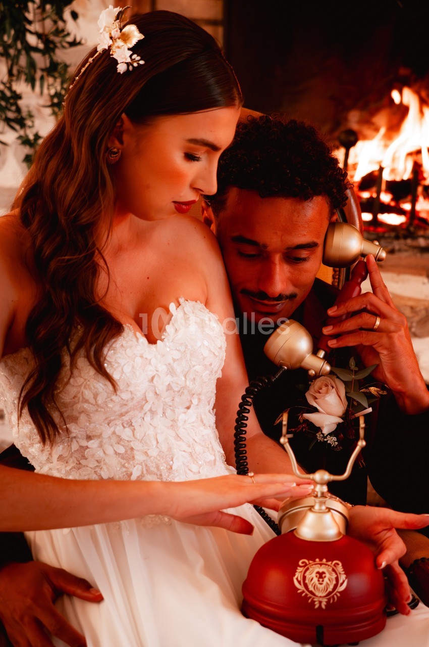 Un couple en tenue élégante partage un moment intime près d'une cheminée, utilisant un téléphone vintage.
