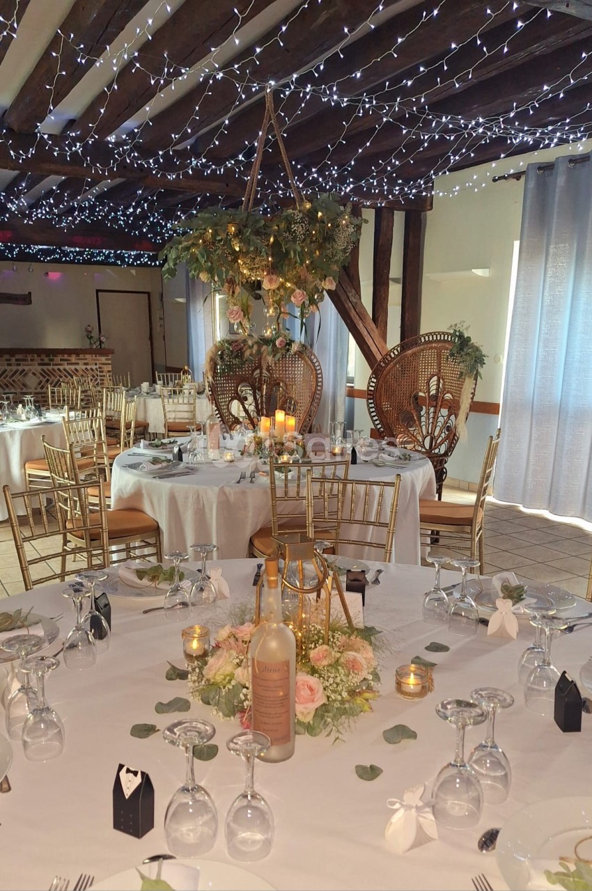 Salle de réception décorée avec des tables rondes, des chaises dorées, des guirlandes lumineuses et des fleurs.