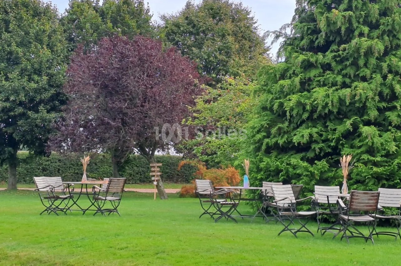 Chaises et tables en métal disposées sur une pelouse verte, entourées d'arbres dans un cadre extérieur paisible.
