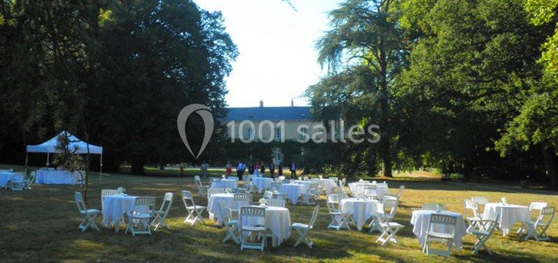 Tables et chaises blanches disposées sur une pelouse devant un bâtiment historique entouré d'arbres.