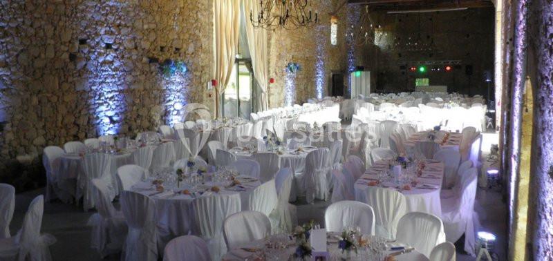Salle de réception en pierre avec tables rondes dressées, nappes blanches et éclairage tamisé.